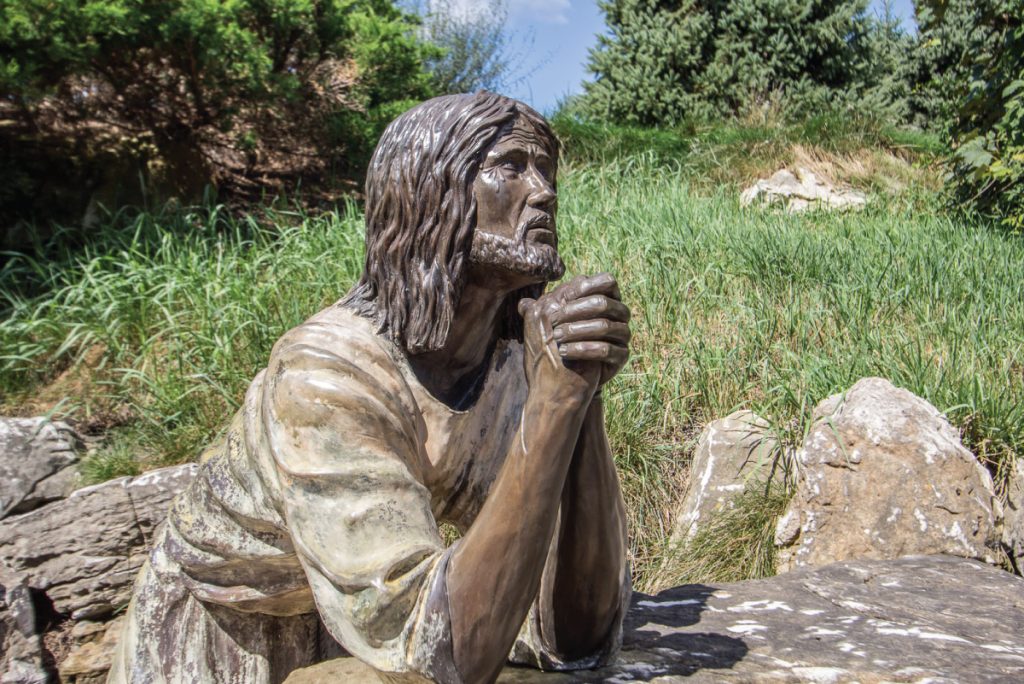 A statue of Jesus kneeling in prayer on a rocky hillside