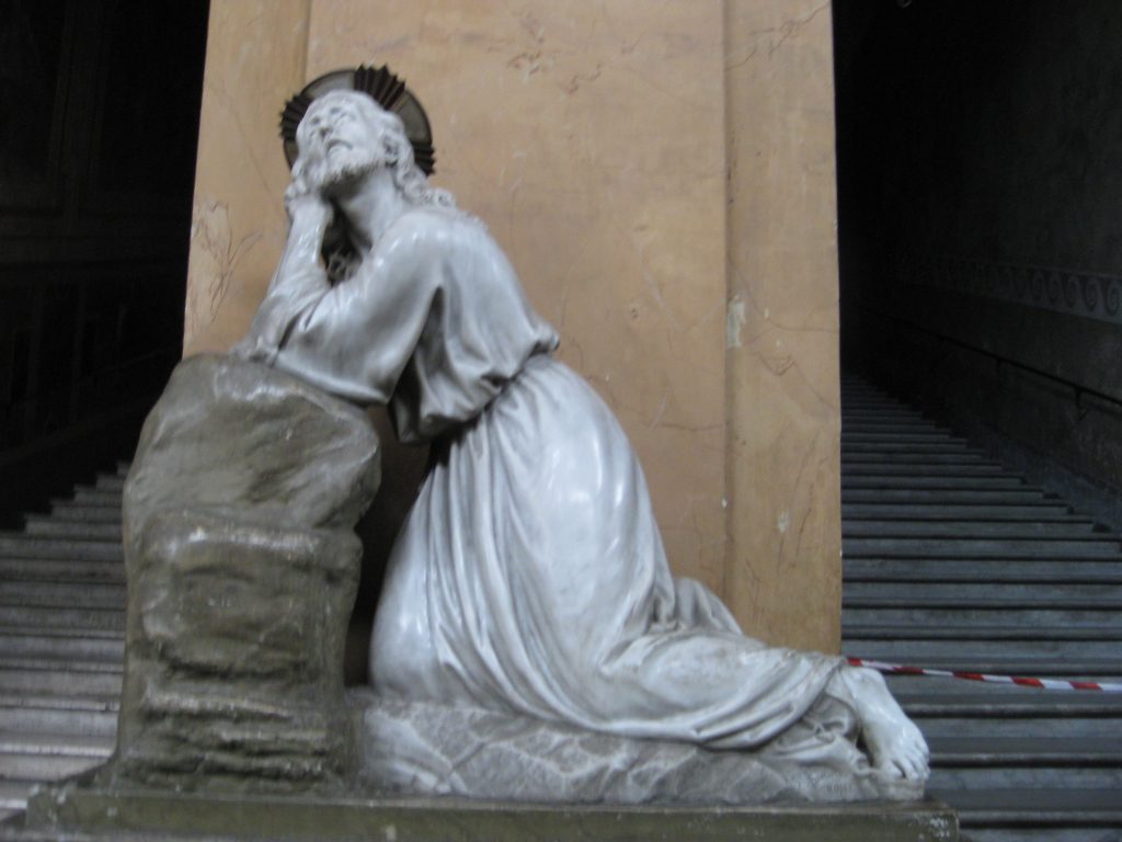 A statue of Jesus praying beside a stone